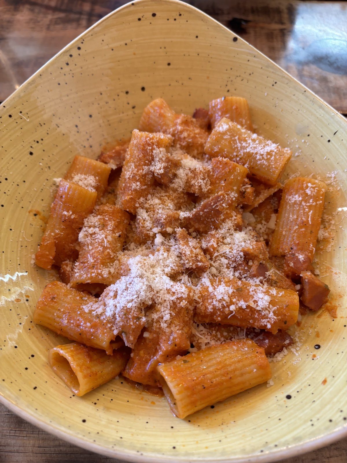 Rigatoni in a rich tomato sauce, snowed with grated cheese, in a speckled mustard-yellow bowl.