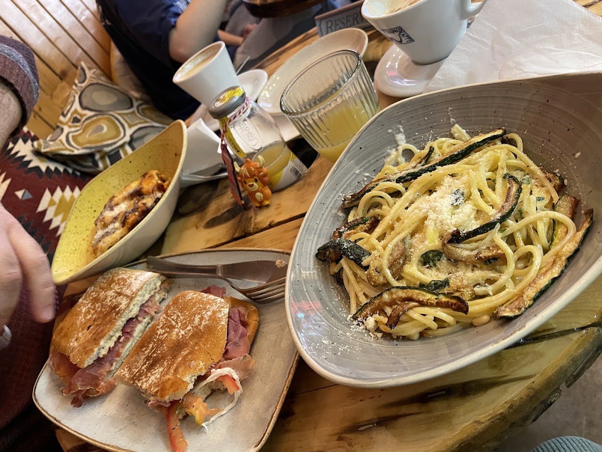 Spaghetti with courgette and cheese in a grey bowl, a toasted panino with cured ham, and a baked pasta in a yellow dish.