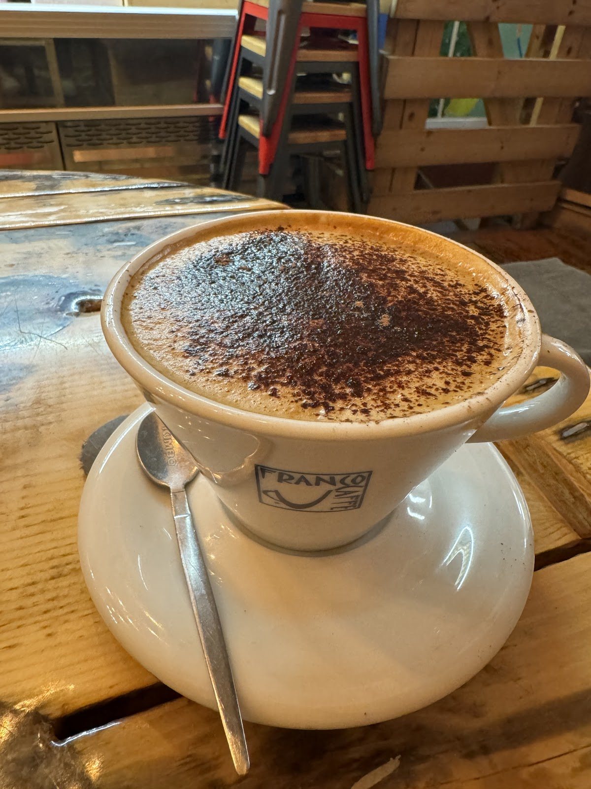 A cappuccino heavily dusted with cocoa in a wide white cup and saucer.